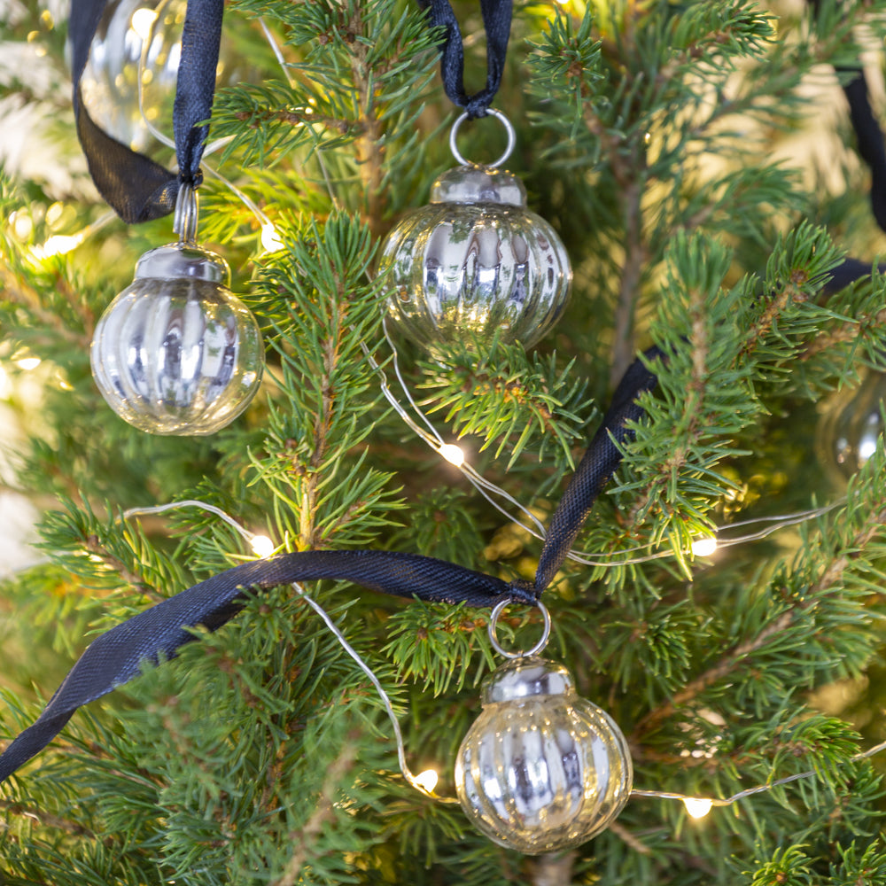 Decorative glass ornaments hanging on a Christmas tree with string lights.