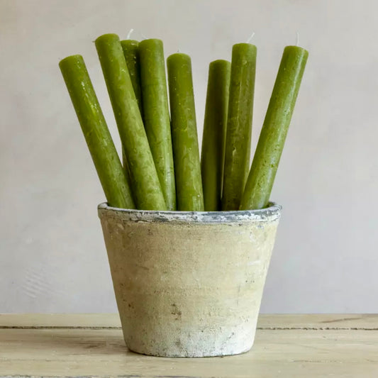 Green candles in a rustic pot on a wooden surface with a neutral background