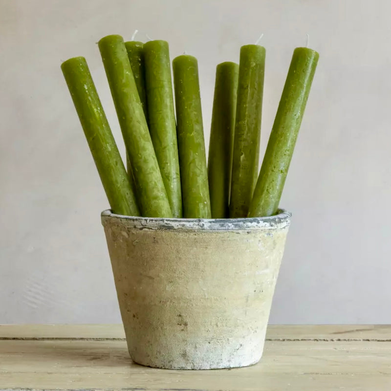 Green candles in a rustic pot on a wooden surface with a neutral background