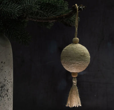 Decorative ornament with jute string and tassel hanging from a branch against a dark background.