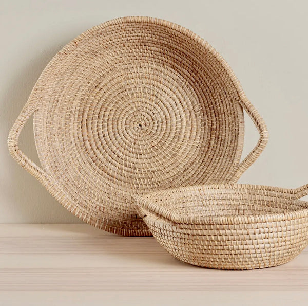 Two woven baskets with handles on a light wooden surface.