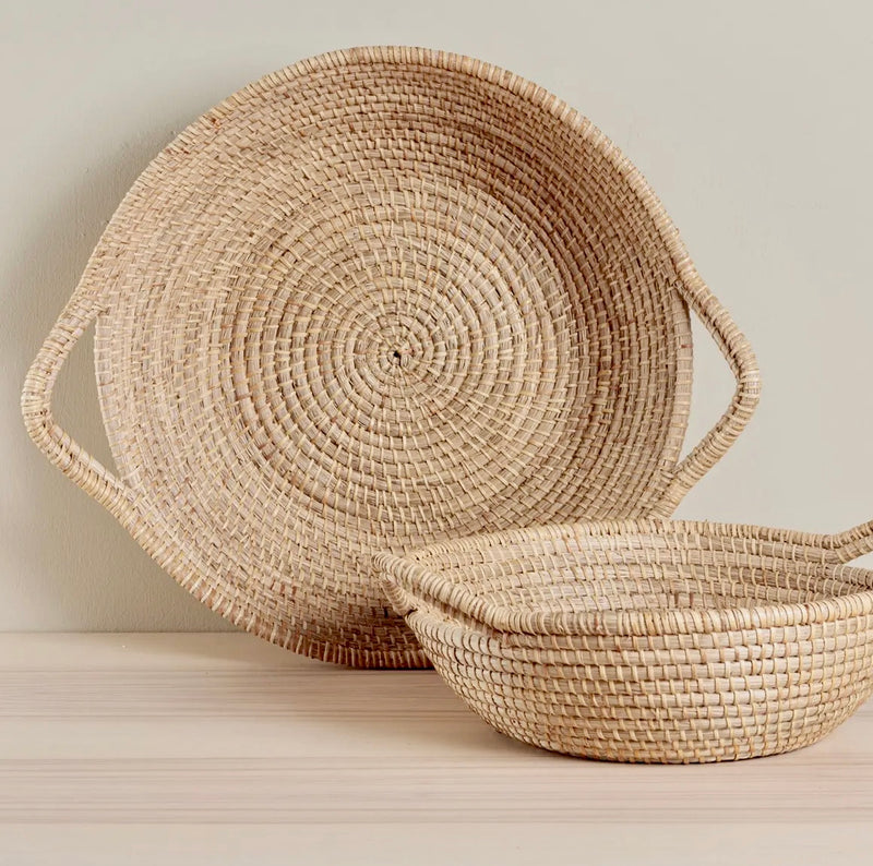 Two woven baskets with handles on a light wooden surface.