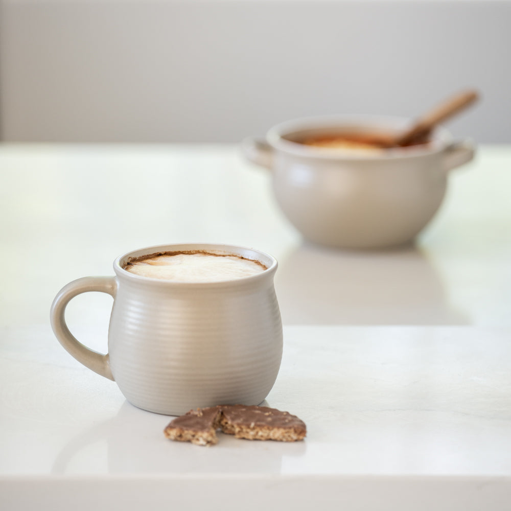 Ceramic mug with a hot beverage on a white surface, accompanied by a bowl and cookies.