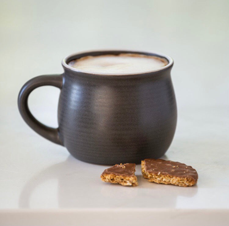 Dark mug with a frothy beverage on a light surface with two cookies.