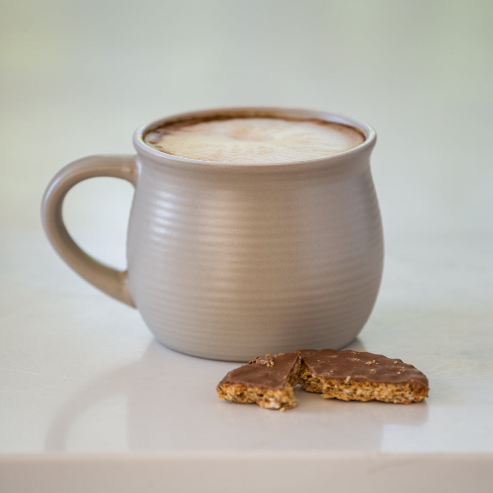 Mug of hot beverage with a cookie on a light surface
