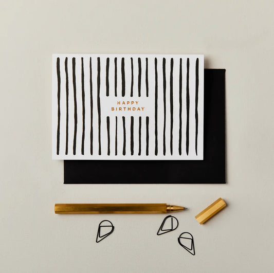 Greeting card with black stripes and 'Happy Birthday' text, accompanied by a pen and envelope on a light gray background.