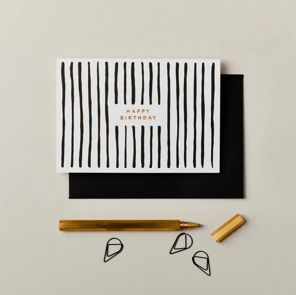 Greeting card with black stripes and 'Happy Birthday' text, accompanied by a pen and envelope on a light gray background.