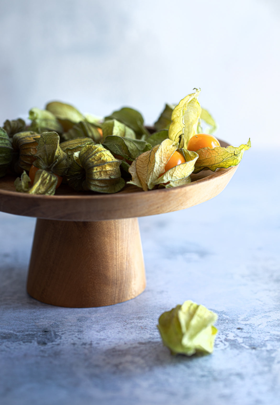Wooden pedestal dish with Physalis on a light background