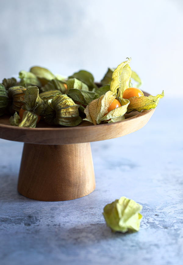 Wooden pedestal dish with Physalis on a light background