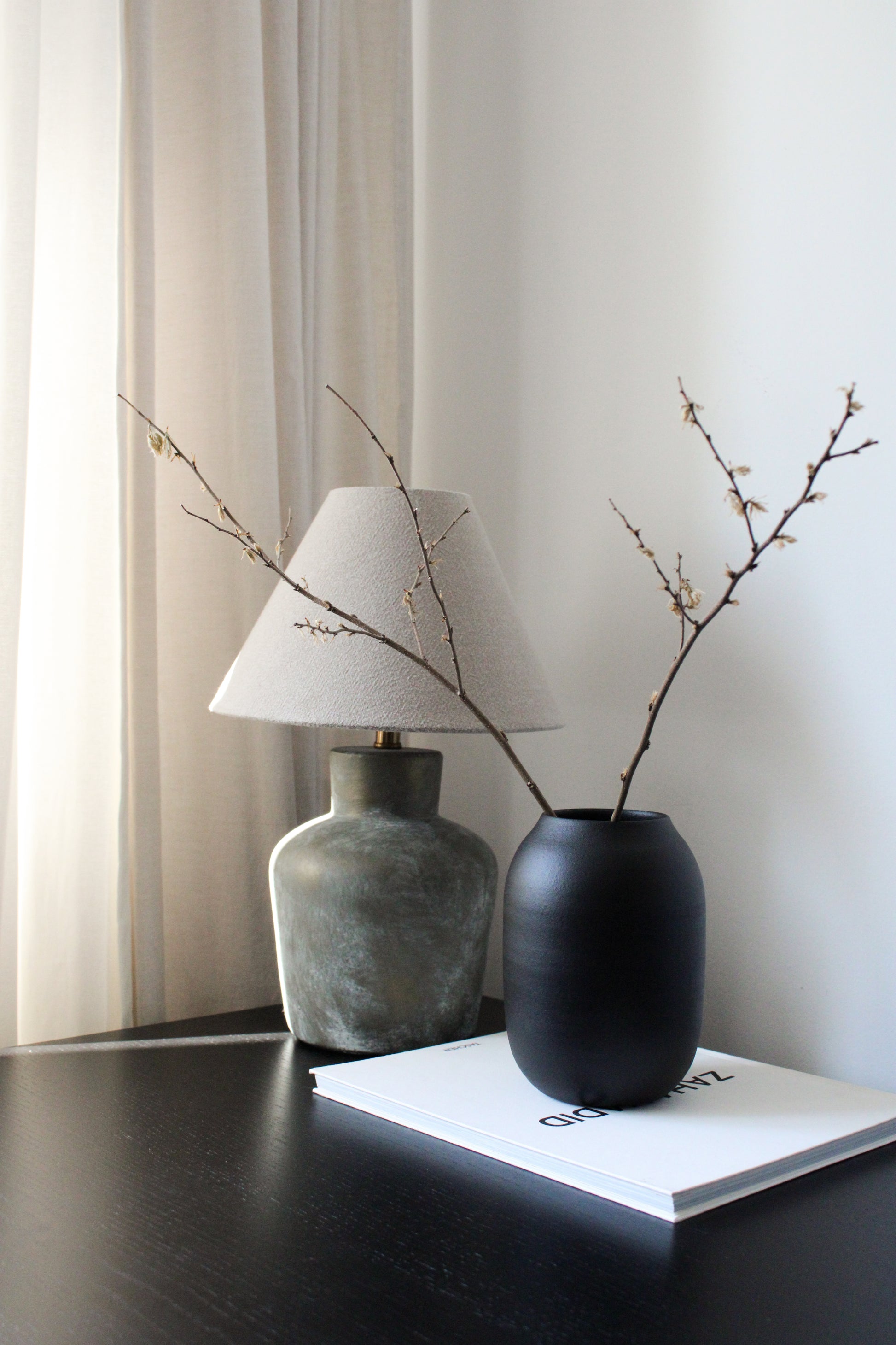 Two vases with branches on a table against a neutral background