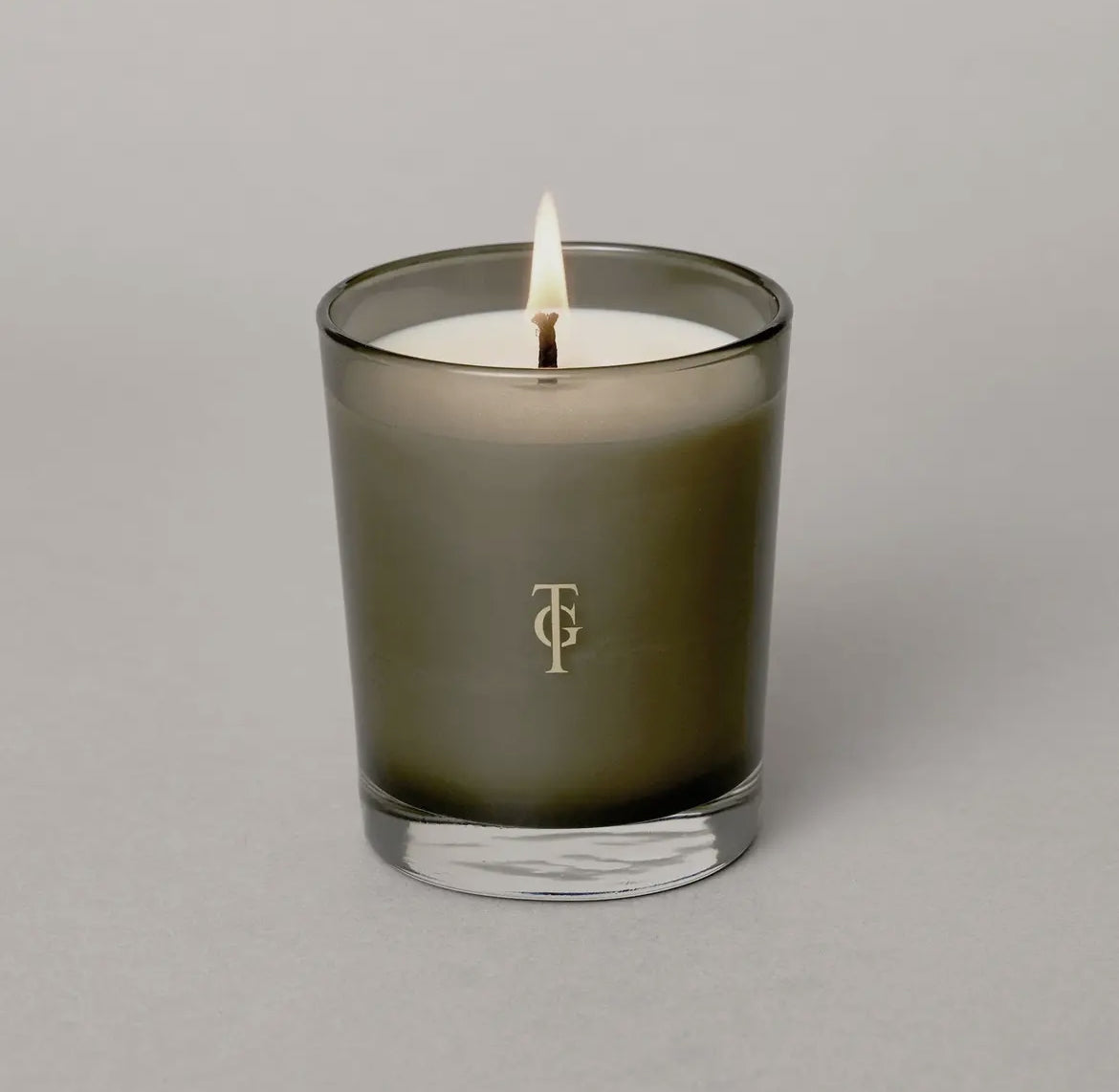 Scented candle in a dark glass container with a logo on a gray background