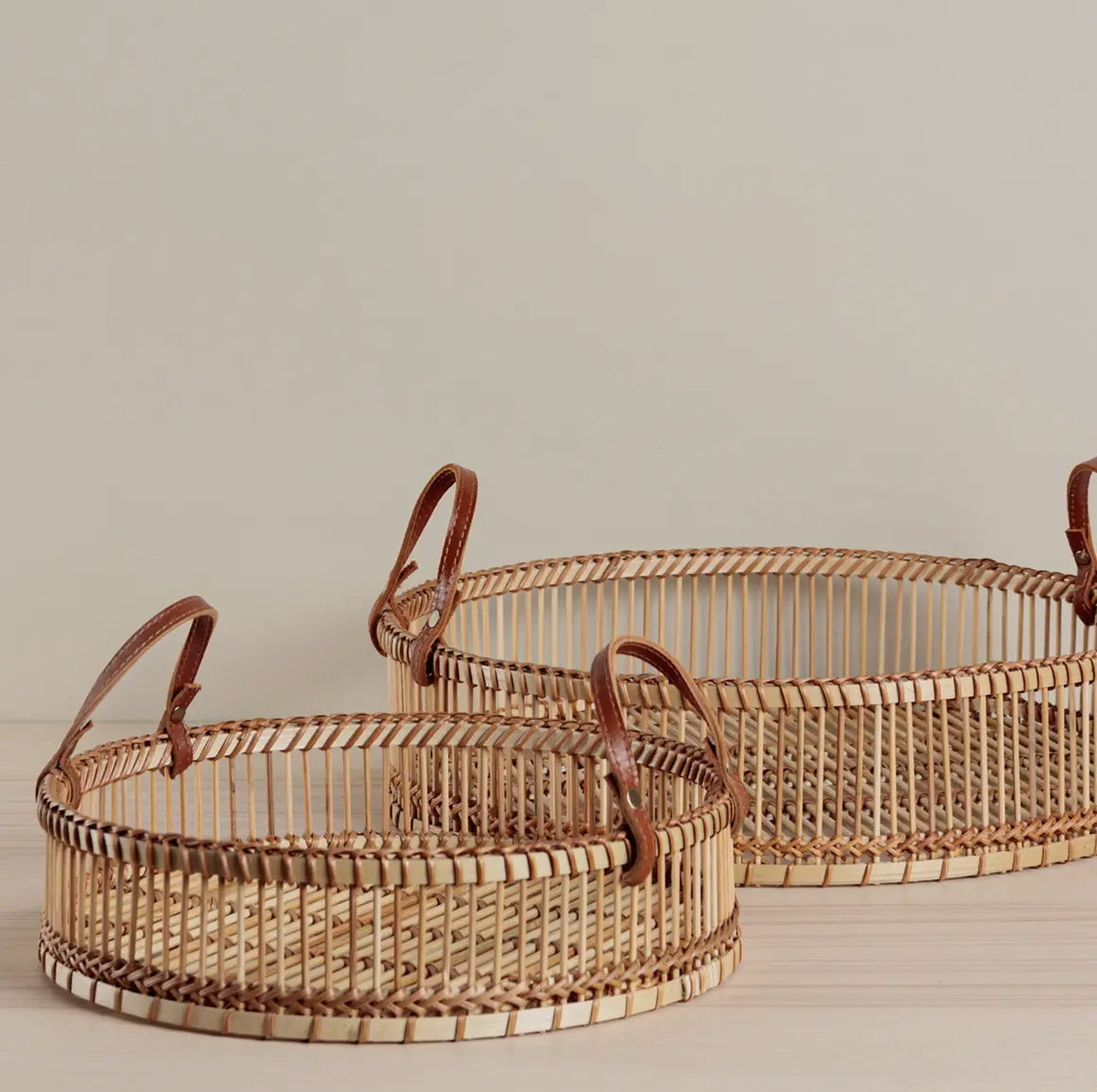 Two woven baskets with leather handles on a neutral background