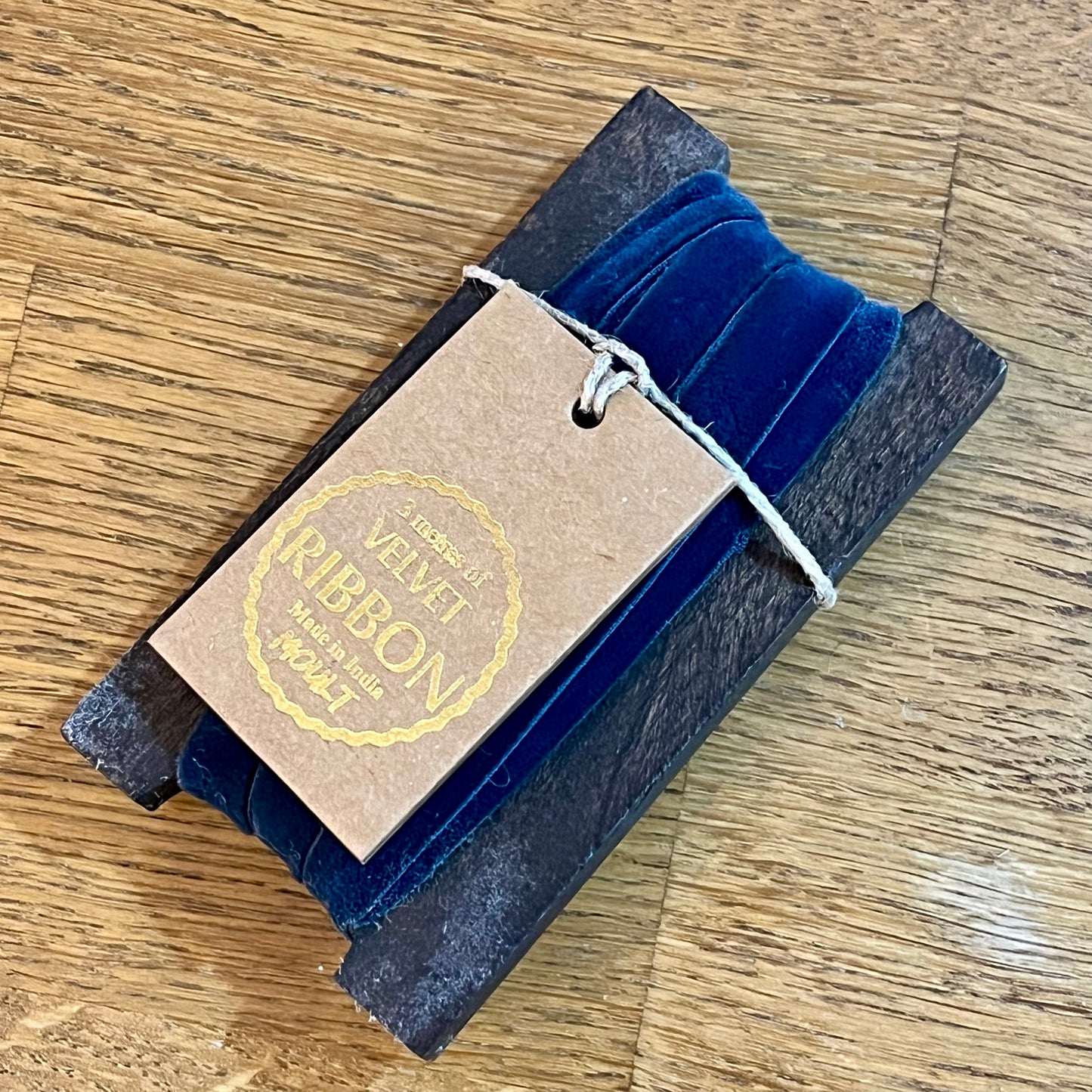 Blue velvet ribbon in a cardboard holder with a label on a wooden surface