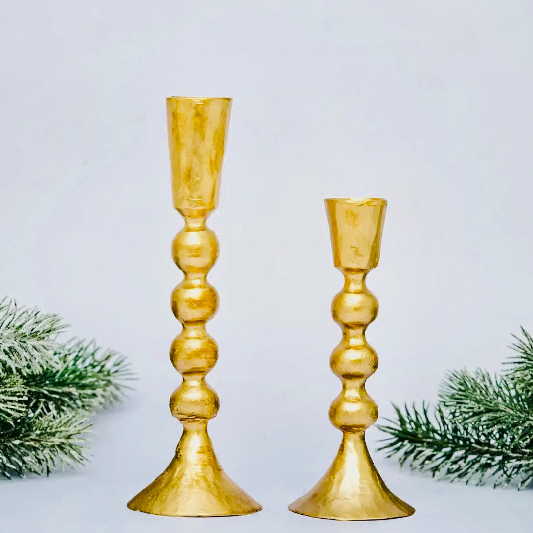 Two gold candle holders with Christmas tree branches on a light gray background