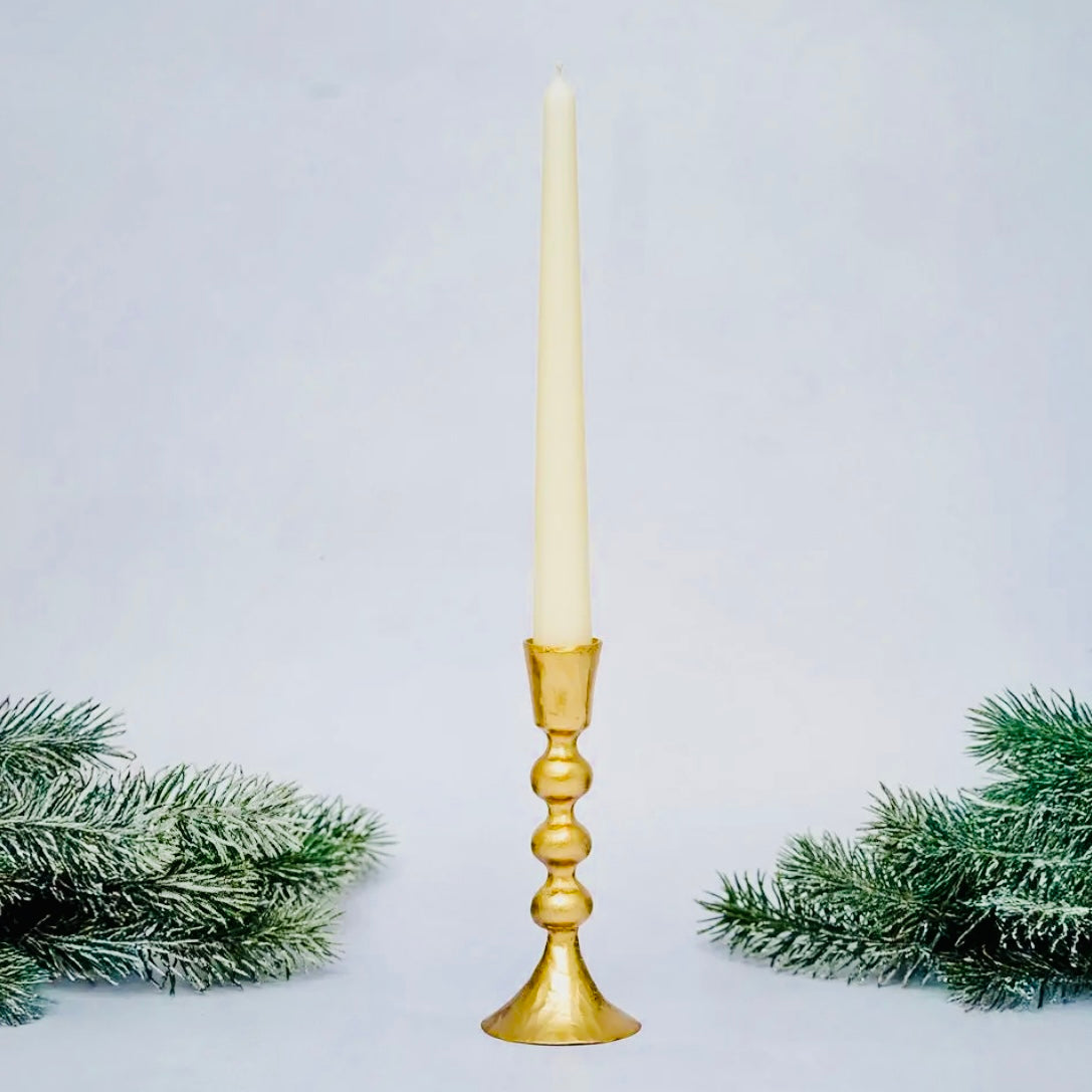 Gold candle holder with a white candle on a light gray background with greenery