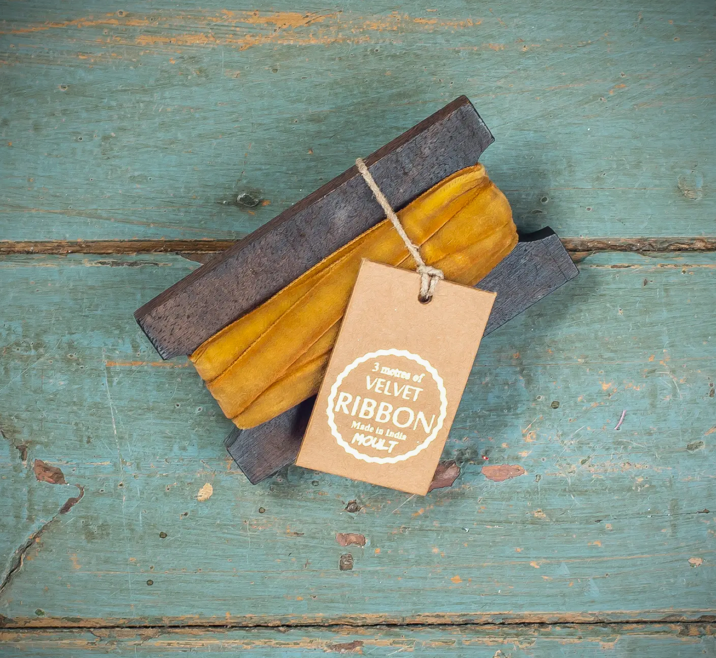 Two pieces of velvet ribbon in gray and mustard yellow with a tag on a rustic wooden surface.